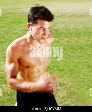 Hübscher junger Mann beim Joggen auf dem grünen Feld. Porträt eines jungen Mannes beim Joggen auf dem grünen Feld - Outdoor. Stockfoto