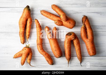 Hässliche Karotten liegen auf einer hellen Holzoberfläche Stockfoto