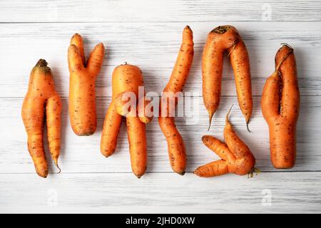 Hässliche Karotten liegen auf einer hellen Holzoberfläche Stockfoto