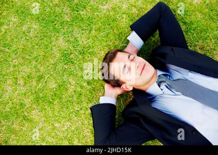 Entspannter junger Geschäftsmann, der friedlich auf dem Gras schläft. Entspannter junger Unternehmer schläft friedlich auf Gras - Copyspace. Stockfoto