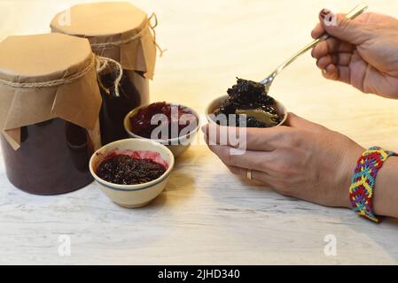 Eine Hand, die hausgemachte Maulbeermarmelade in kleinen Schüsseln aus Gläsern serviert Stockfoto