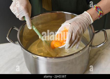 Hände in Gummihandschuhen, die Teig für einen Kuchen in einem Topf rühren Stockfoto