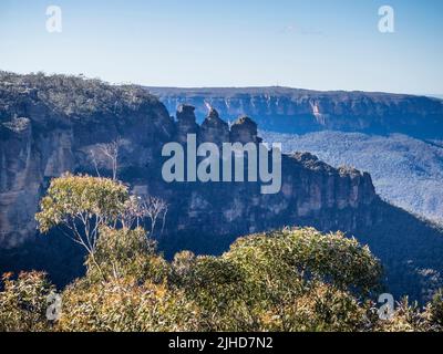 Die drei Schwestern und das Jamison Valley an einem sonnigen Wintermorgen mit der Sandsteinwand des Königstableland im Hintergrund, Katoomba, Blue Mountains Stockfoto