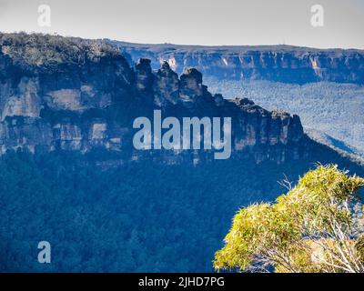 Die drei Schwestern und das Jamison Valley an einem sonnigen Wintermorgen mit der Sandsteinwand des Königstableland im Hintergrund, Katoomba, Blue Mountains Stockfoto