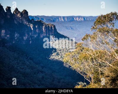 Die Three Sisters und Jamison Valley an einem sonnigen Wintermorgen liegen die Sandsteinwände von Kings Tableland in der Ferne. Katoomba, Blue Mountains. Stockfoto