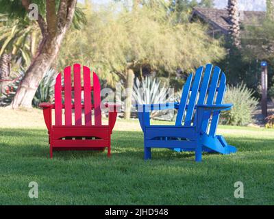 Rote und blaue Adirondack-Stühle auf Rasen - Morgen Stockfoto