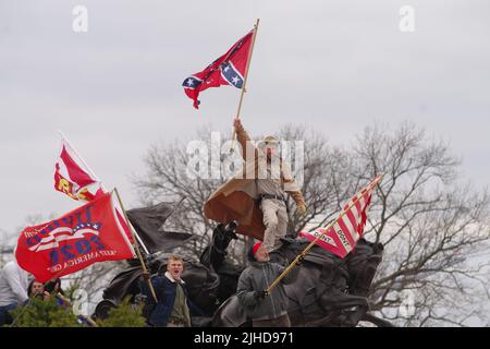 Während der Unruhen am 6. Januar 2021 winkt ein Mann auf einer Statue in der Nähe des US-Kapitols mit einer konföderierten Flagge. Stockfoto