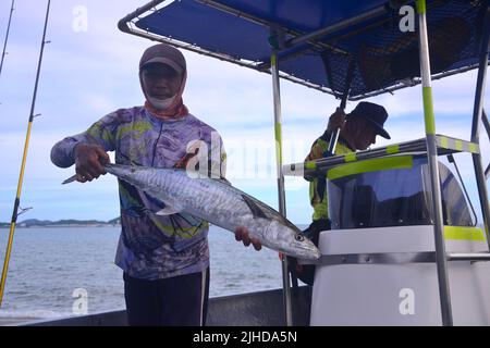 Ein Fischer hält stolz einen großen Fisch hoch, den er auf einem Fischerboot in Thailand, Asien, gefangen hat. Stockfoto