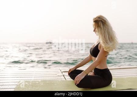 Eine junge Frau praktiziert Yoga an der Meeresküste während des Sonnenaufgangs. Stockfoto