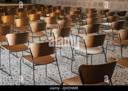 Set von leeren Holzstühlen aufgereiht vor einer Veranstaltung in einer alten Kirche oder Burg mit mittelalterlichen Boden und Wänden. Selektiver Fokus. Stockfoto
