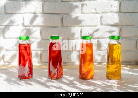 Reihe von Glasflaschen mit verschiedenen Säften gegen weiße Ziegelwände Stockfoto