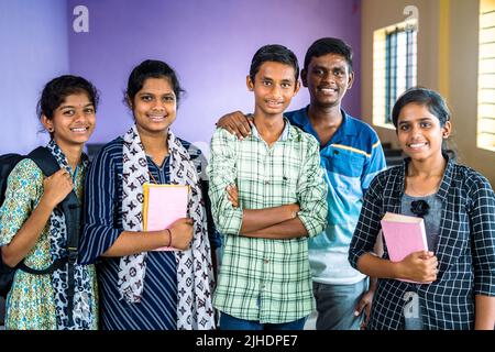 Gruppe von Studenten selbstbewusst stehen mit Büchern und Rucksack im Klassenzimmer durch Blick auf Kamera - Konzept der Bildung, Freundschaft und Stockfoto