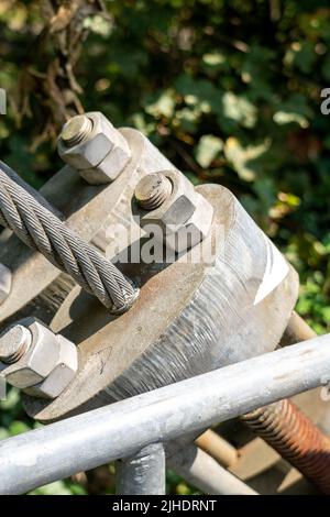 Schraube mit Mutter, mit der das Seil einer Hängebrücke mit einem verdrehten Stahlkabel in Nahaufnahme befestigt wird. Schweres Engineering-Konzept Stockfoto