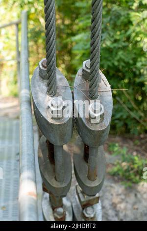 Schraube mit Mutter, mit der das Seil einer Hängebrücke mit einem verdrehten Stahlkabel in Nahaufnahme befestigt wird. Schweres Engineering-Konzept Stockfoto