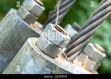 Schraube mit Mutter, mit der das Seil einer Hängebrücke mit einem verdrehten Stahlkabel in Nahaufnahme befestigt wird. Schweres Engineering-Konzept Stockfoto