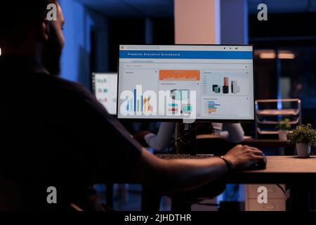 Junger Geschäftsmann, der Computermonitor mit Diagrammen betrachtet, statistische Informationen und Daten analysiert, um Projektbericht zu erstellen, Finanzforschung durchführt. PC-Bildschirm mit Netzwerkdarstellung. Stockfoto