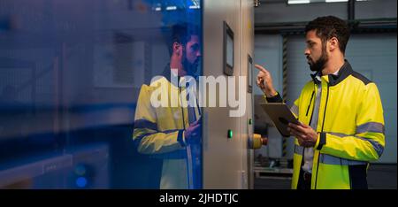Junger Industriearbeiter, der CNC-Maschine bei der Metallbearbeitungsindustrie betreibt Stockfoto