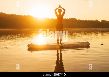 Eine Frau kühlt sich an einem heißen Sommertag durch Yoga auf dem Paddle Board ab. Stockfoto