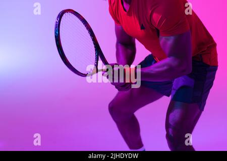 Bild des Mittelteils des afroamerikanischen Tennisspielers in neonvioletter Beleuchtung Stockfoto