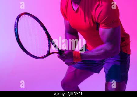 Bild des Mittelteils des afroamerikanischen Tennisspielers in neonvioletter Beleuchtung Stockfoto