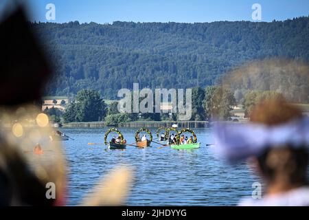 Radolfzell Am Bodensee, Deutschland. 18.. Juli 2022. Mit Blumenkränzen geschmückte Boote fahren während der Moos-Wasserprozession über den Bodensee zum Ufer von Radolfzell, während Frauen in ihren traditionellen Kostümen am Ufer stehen. Die Prozession fand erstmals 1926 auf dem Wasser über den Bodensee statt. Es stammt aus dem 18.. Jahrhundert. 1796 wurden die Bürger von Moos von einer Viehpest verschont - aus Dankbarkeit dafür findet die Veranstaltung jedes Jahr am dritten Montag im Juli statt. Quelle: Felix Kästle/dpa/Alamy Live News Stockfoto