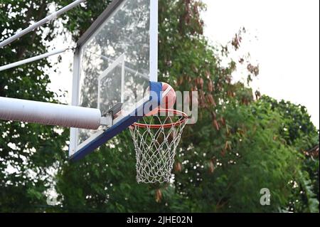 Ein Basketballball, der in einem Park voller Bäume mit grünen Blättern ins Netz geht Stockfoto