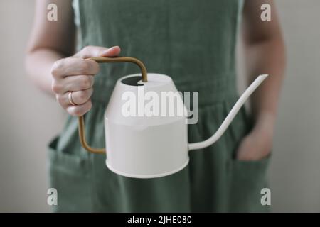 Mädchen in Schürze hält eine Gießkannel. Bewässerung und Pflege für Heimpflanzen. Home Gartenarbeit. Hobby-Blumen-Anbau Stockfoto