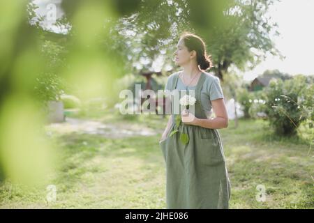 Gartenarbeit und Berufskonzept - junge Frau im Schürze hält Blumen im Garten im Sommer Stockfoto