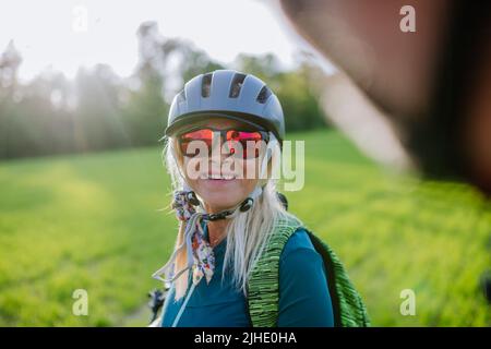 Aktives Seniorenpaar, das auf der Straße im Sommerpark Elektrofahrräder fährt, gesundes Lifestyle-Konzept. Stockfoto