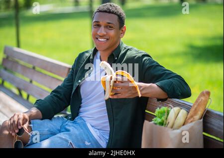 Ein lächelnder Kerl, der die Kamera auf der Bank anschaut Stockfoto