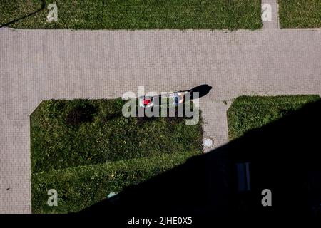 Mann schiebt Rasenmäher für das Schneiden von grünem Gras im Garten im Sommer. Luftaufnahme. Stockfoto