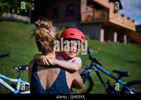 Junge Mutter mit kleiner Tochter, die sich auf die Fahrradtour vorstellt, Helme aufsetzt und umarmt. Stockfoto