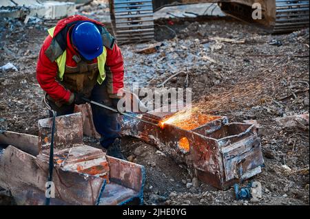 Ein Mitarbeiter im Helm schneidet alte Metallbalken für das Recycling vor Ort Stockfoto