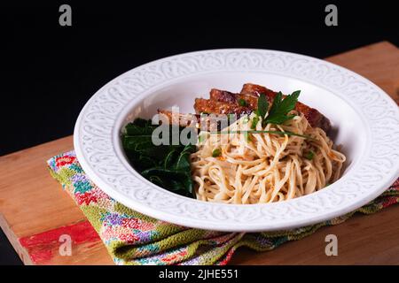 Asiatisches Food-Konzept hausgemachte Bio-Alkaline-Nudeln mit Ente auf Holzbrett mit schwarzem Hintergrund mit Kopierraum geröstet Stockfoto