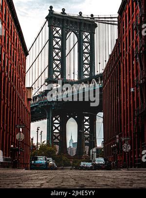 Ikonisches Foto von Dumbo Manhatten. Zwischen den Pillern der Manhetten-Brücke ist das Empire State Building zu sehen. Stockfoto