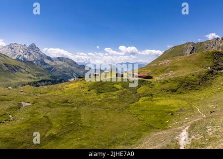 Luftaufnahme einer sehr großen und majestätischen alpinen Landschaft im Herr der Ringe Stil. In der Mitte befindet sich ein kleines Bergdorf, das hauptsächlich aus Almen besteht. Stockfoto