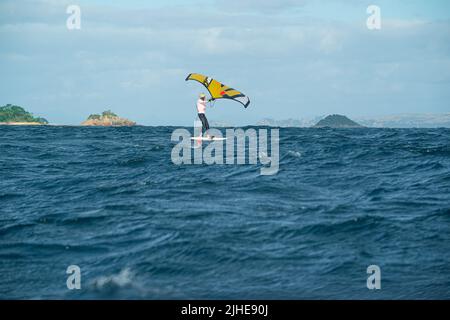 Ein Mann Flügel Folien auf dem Meer mit einem Hand gehalten aufblasbaren Flügel, Reiten ein Tragflächenboot Surfboard Flügel Folie Bord. Hauraki Gulf, Auckland, Neuseeland. Stockfoto