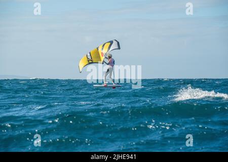 Ein Mann Flügel Folien auf dem Meer mit einem Hand gehalten aufblasbaren Flügel, Reiten ein Tragflächenboot Surfboard Flügel Folie Bord. Hauraki Gulf, Auckland, Neuseeland. Stockfoto