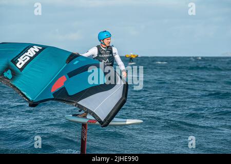 Ein Mann Flügel Folien auf dem Meer mit einem Hand gehalten aufblasbaren Flügel, Reiten ein Surfbrett. Hauraki Gulf, Auckland, Neuseeland. Stockfoto