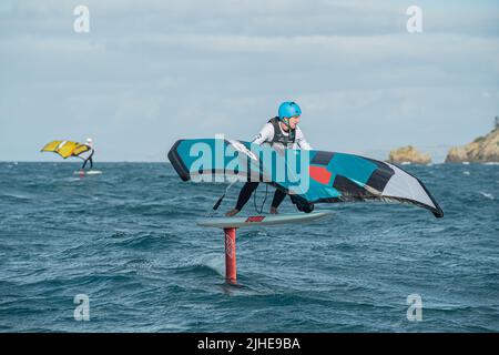 Ein Mann Flügel Folien auf dem Meer mit einem Hand gehalten aufblasbaren Flügel, Reiten ein Surfbrett. Hauraki Gulf, Auckland, Neuseeland. Stockfoto