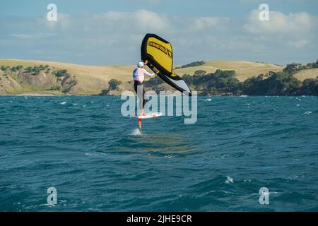 Ein Mann Flügel Folien auf dem Meer mit einem Hand gehalten aufblasbaren Flügel, Reiten ein Tragflächenboot Surfboard Flügel Folie Bord. Hauraki Gulf, Auckland, Neuseeland. Stockfoto