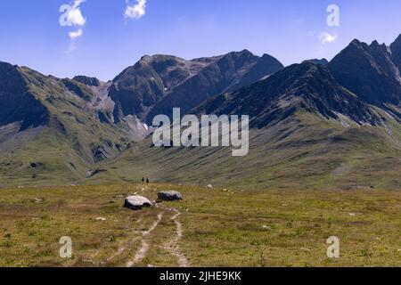 Zwei Frauen wandern im Spätsommer an einem sonnigen Tag auf dem Greina Plateau in der Schweiz auf einem kurvenreichen Alpinpfad zwischen den Bergen. Hochwertige Fotos Stockfoto