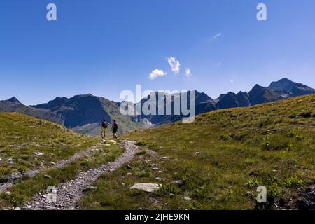 Zwei Frauen wandern im Spätsommer an einem sonnigen Tag auf dem Greina Plateau in der Schweiz auf einem kurvenreichen Alpinpfad zwischen den Bergen. Hochwertige Fotos Stockfoto