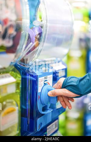 Eine menschliche Hand in einem türkisfarbenen Pullover dreht eine blaue Gashapon-Maschine, um eine Figur freizugeben. In Japan gilt sie als eine der beliebtesten Stockfoto