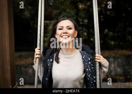 Porträt einer jungen lächelnden Frau, die im Wald auf Schaukel sitzt Stockfoto