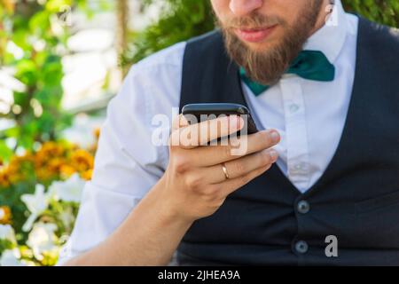 Nahaufnahme auf einem Smartphone in der Hand eines bärtigen Hipsters in einem Anzug, Sommer im Freien Stockfoto