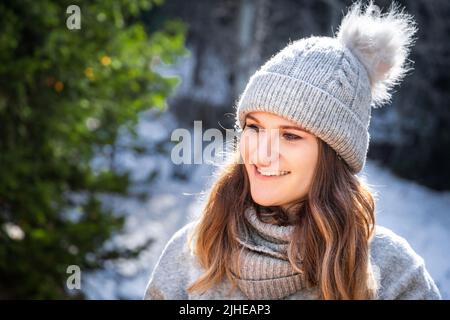 Winterportrait der kaukasischen blonden jungen lächelnden Frau in grauem Pullover und Mütze Hut im Freien Stockfoto