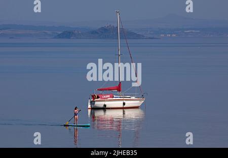 Portobello, Edinburgh, Schottland, Großbritannien. 18.. Juli 2022. Die Temperatur stieg mit 23 Grad Celsius nur after10am, stieg bis 1pm sogar auf 29 Grad Celsius. Im Bild: Cooler Paddlebarder, der den ruhigen Firth of Forth mit Inchkeith Island im Hintergrund genießt. Stockfoto