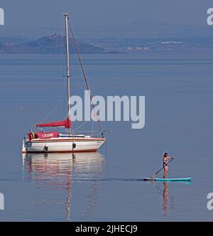 Portobello, Edinburgh, Schottland, Großbritannien. 18.. Juli 2022. Die Temperatur stieg mit nur after10am Grad Celsius um 23 Grad Celsius und stieg bis 1pm auf 29 Grad Celsius. Im Bild: Cooler Paddlebarder, der den ruhigen Firth of Forth mit Inchkeith Island im Hintergrund genießt. Stockfoto