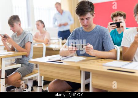 Die Schüler benutzen Mobiltelefone und schreiben in Notizblöcke während der Nahaufnahme des Unterrichts Stockfoto